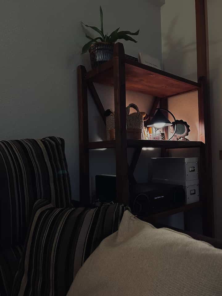 Cozy living room with dark brown wood-toned shelves and a black table lamp, featuring a striped sofa and beige cushion