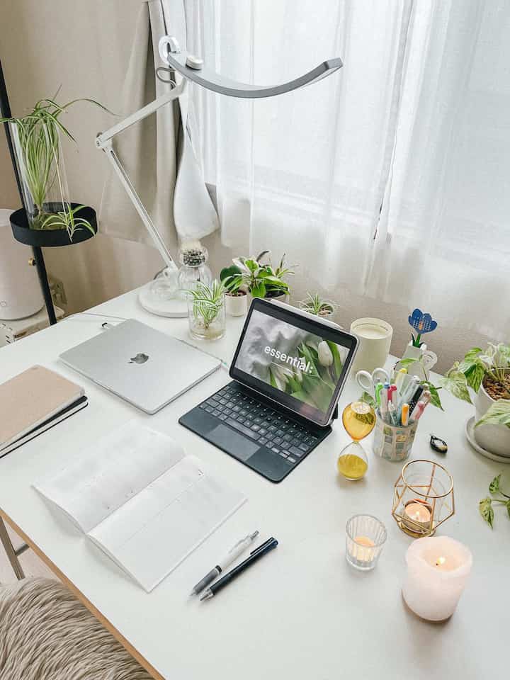 白を基調としたホームオフィス空間、デスク上にノートパソコン、アイパッド、小さな植物とキャンドルが配置されたシンプルで落ち着いたワークスペース