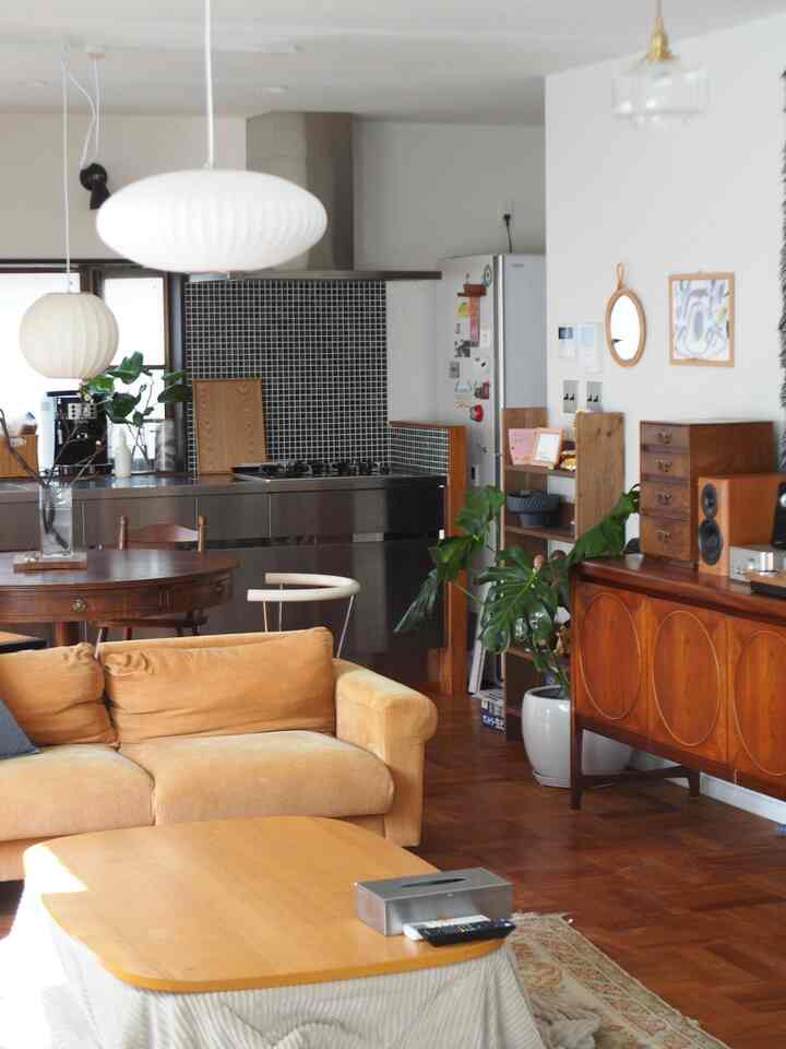 ミッドセンチュリーモダン家具とステンレスキッチンが調和した、木目調の床と白い壁のリビング空間