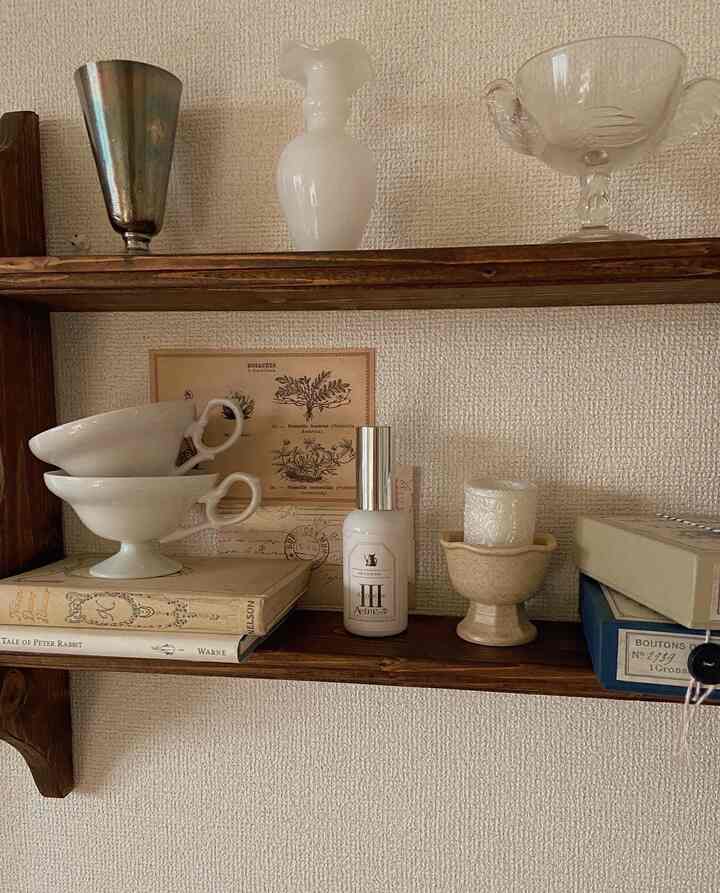 ナチュラルなブラウンの木製棚に白い陶器のカップやガラスの花瓶、香水やキャンドルが配置された雰囲気あるインテリア小物の空間