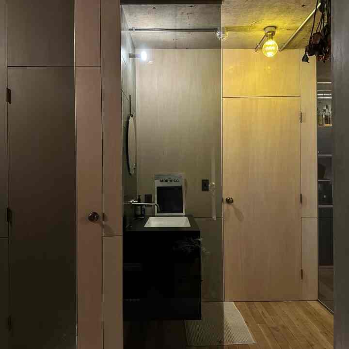 Modern bathroom featuring light wood tone walls and dark black sink vanity with transparent glass partition