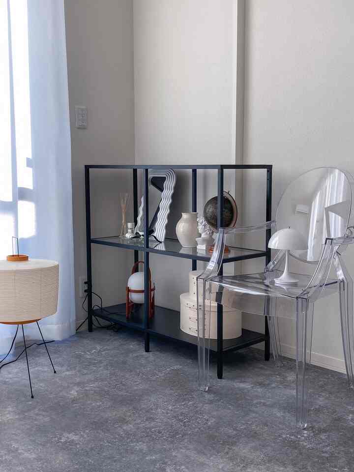 モノトーンのリビング、透明なアームチェアと黒い棚、自然光が差し込むシンプルな雰囲気のインテリア