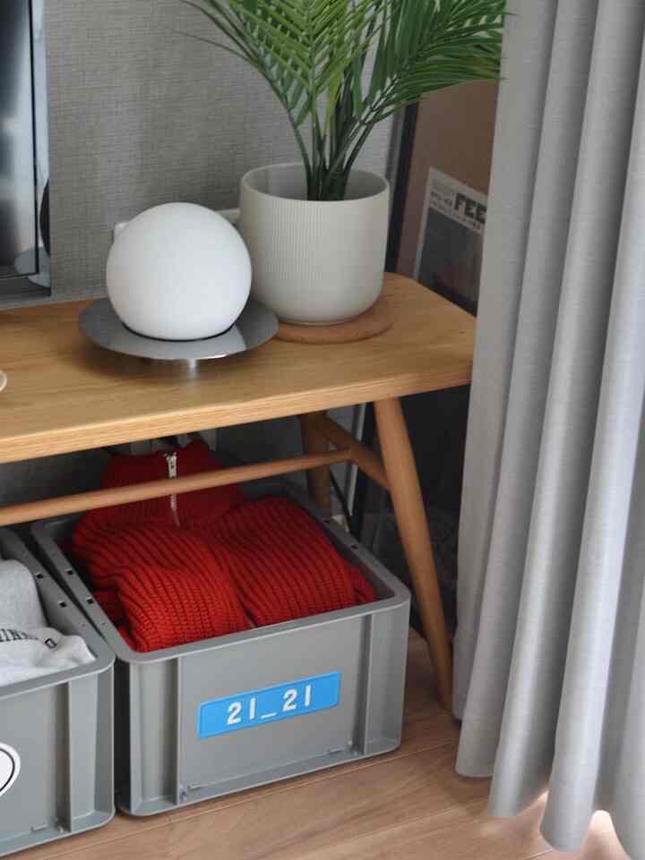 ナチュラルな木製ベンチの下にグレーの収納ボックスとグレーのカーテンがあるコンパクトな6畳の一人暮らし空間