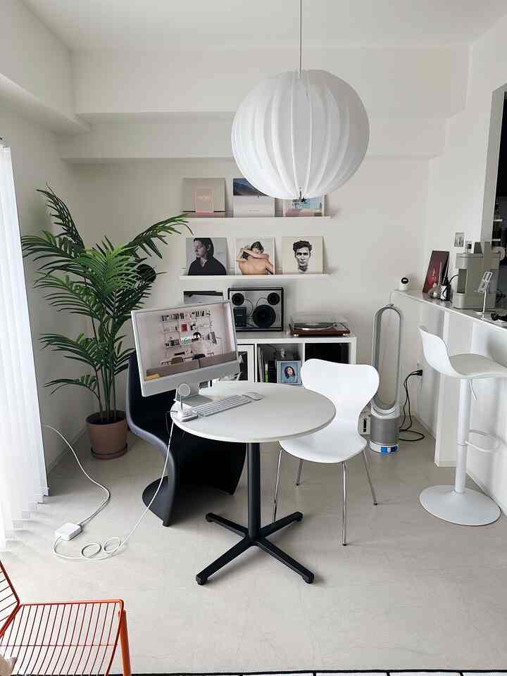 White-toned modern compact dining room featuring a round table, black and white chairs, and a large pendant light