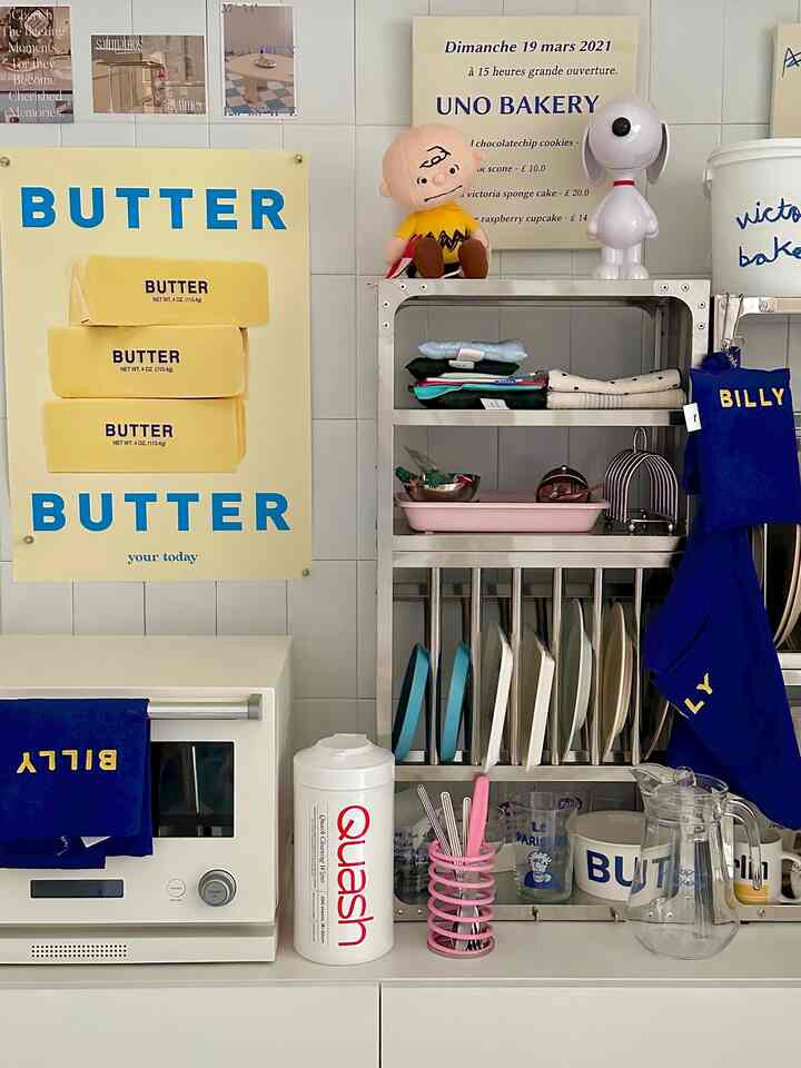White and blue toned kitchen space featuring a stainless steel rack and posters arranged neatly with a clean aesthetic