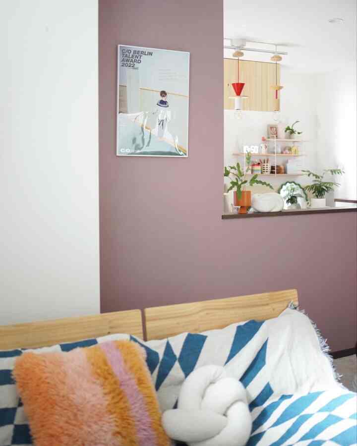 A living room with pink and white walls featuring a wood-tone sofa with colorful cushions and pendant lights, creating a cozy atmosphere.