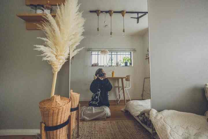 ベージュとナチュラルカラーのワンルーム、全身鏡と木製のダイニングテーブル、ラタンバスケットが配置された雰囲気のあるインテリア