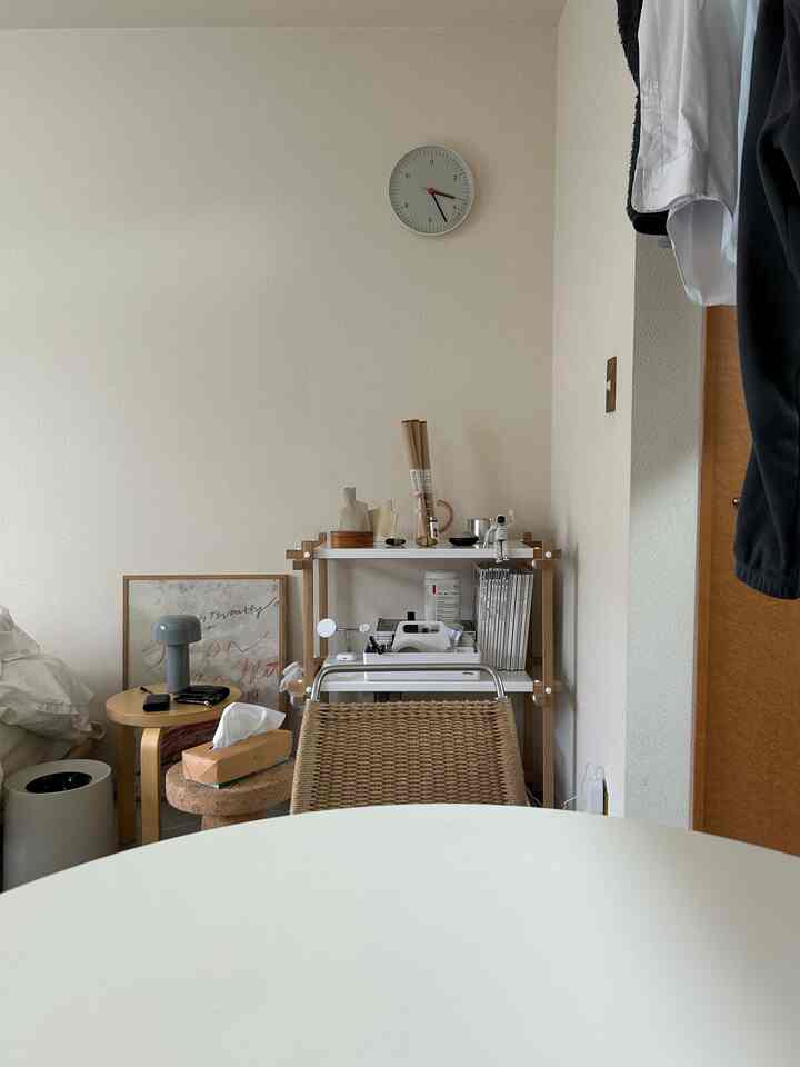 白とナチュラルな色調の狭いリビング、丸テーブルとサイドテーブル、壁時計が配置されたミニマルで落ち着いたインテリア