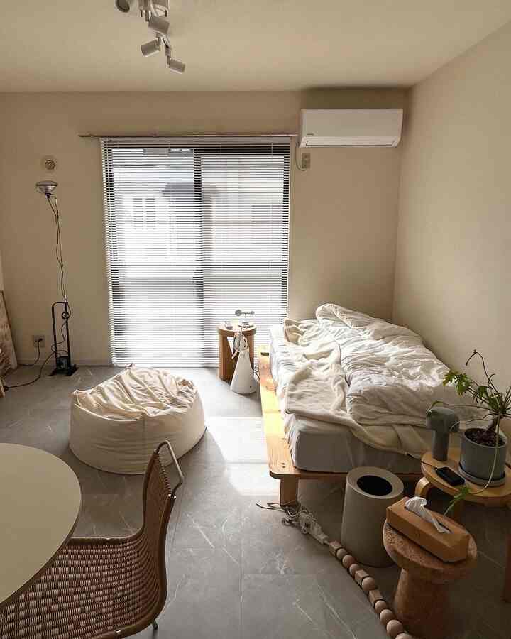 ホワイトとナチュラルな色調の一人暮らし用の小さな部屋、木製ベッドとビーンバッグ、スツールが配置された落ち着いたインテリア