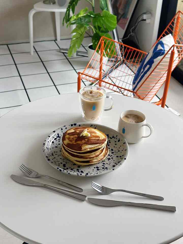 白とオレンジのシンプルなホームカフェ空間、ブルーボトルのマグと大理石模様の皿にパンケーキが載ったテーブル