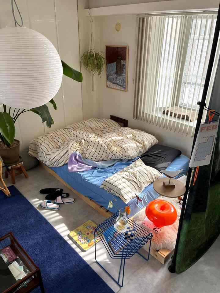 ホワイトとブルーの色調の寝室、ナチュラルな木製ベッドと植物、サイドテーブルが配置された雰囲気のあるインテリア