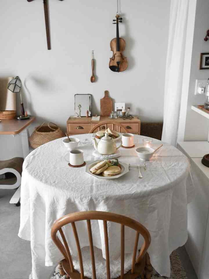 白いテーブルクロスが掛けられた円形のダイニングテーブルとナチュラルな木製家具が配置された、アットホームな二人暮らし向けのフレンチカントリースタイルのダイニングルーム