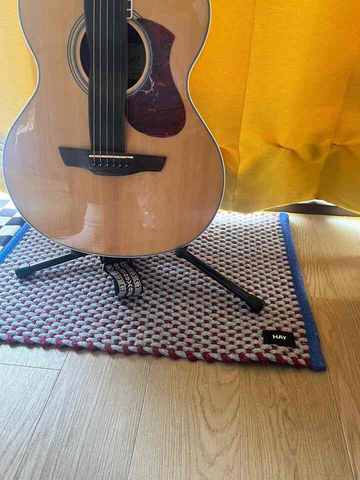 Entrance space featuring gray and red door mat with guitar placed on wood tone floor and yellow curtain in background