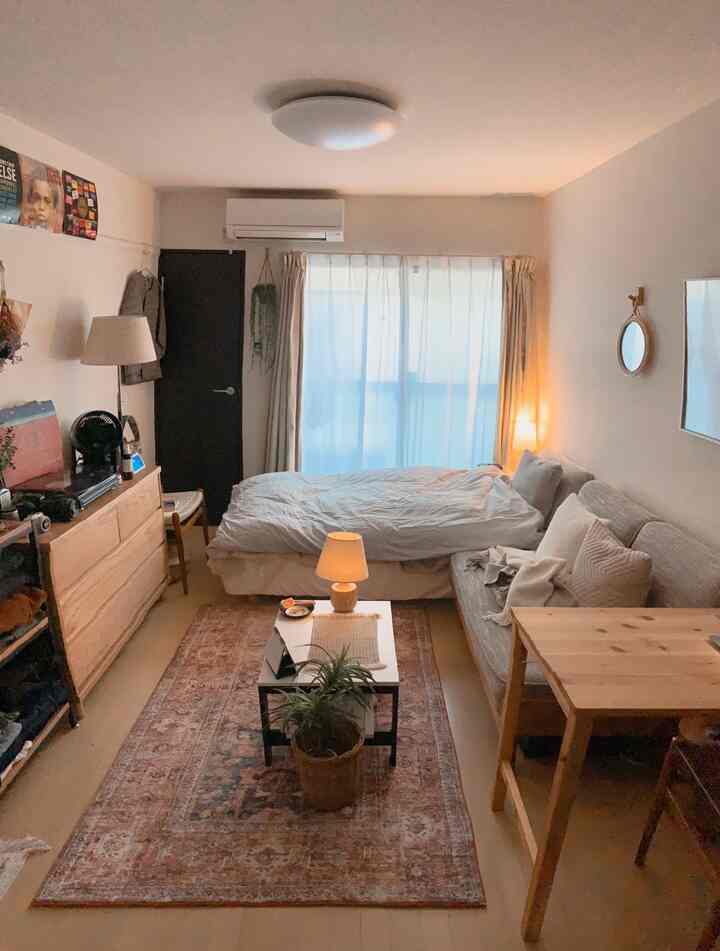 ナチュラルな色調の一人暮らしの寝室、木製家具とヴィンテージラグ、そして温かみのある間接照明が配置された雰囲気のあるインテリア