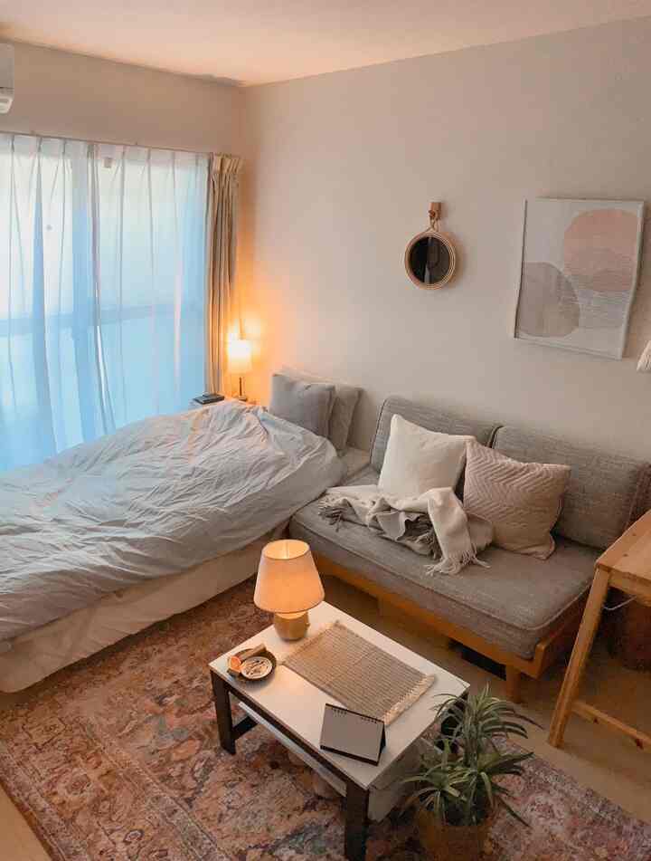 柔らかなベージュ調のワンルーム寝室、ナチュラルなソファとテーブルランプが配置された雰囲気のあるインテリア