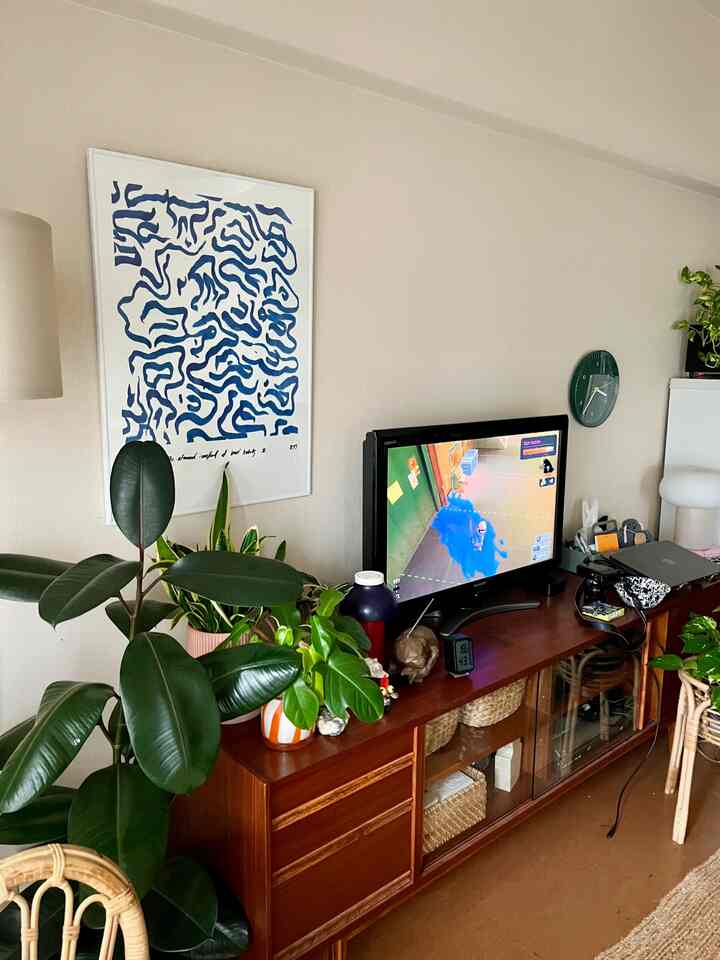 ブラウンの木目調が際立つリビング、大型の植物とテレビ台、ゲーム画面が配置された自然な雰囲気の空間