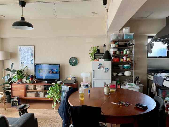 Beige background with wood-tone round dining table, TV stand, and kitchen combined in a natural modern dining room for two