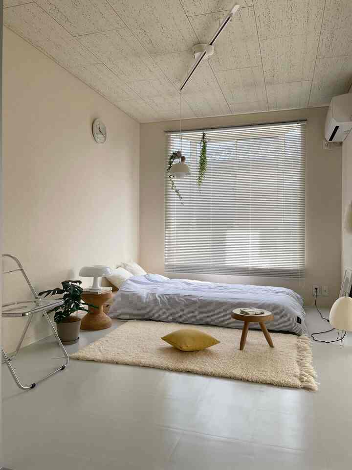 Beige and white toned bedroom featuring low bed, rug, plant, and stool creating a cozy atmosphere