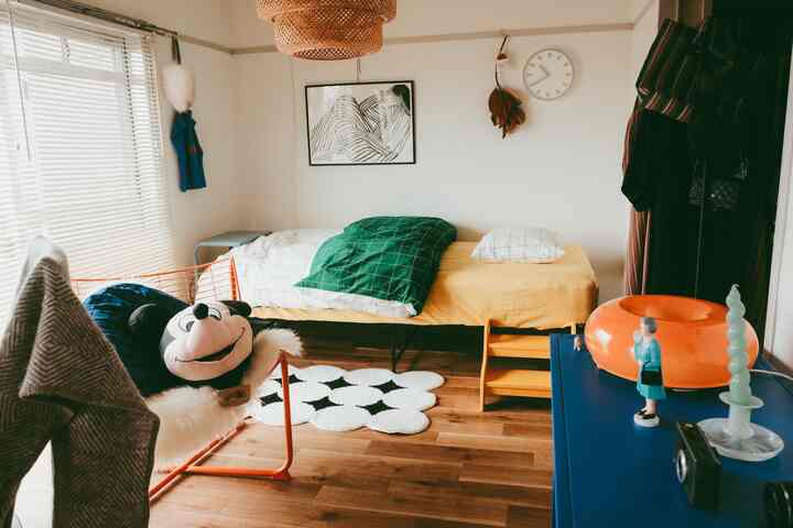 Natural-toned compact modern bedroom featuring orange armchair and blue storage cabinet with cozy atmosphere