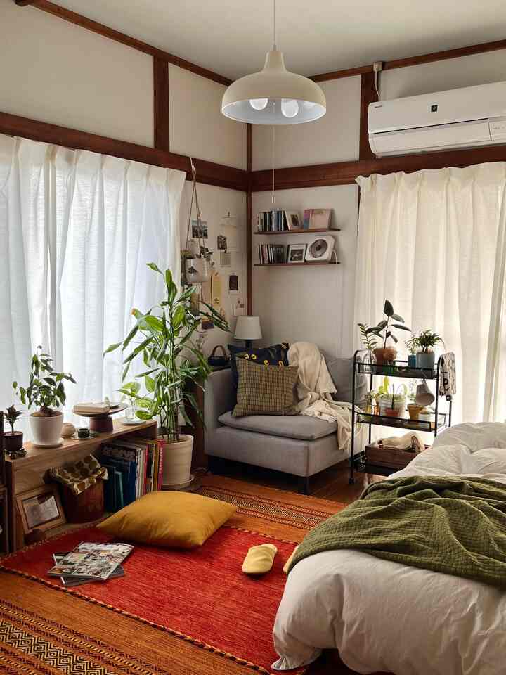 ホワイトカーテンとライトグレーのソファ、複数の植物が配置されたナチュラルモダンスタイルの小さな一人暮らしのリビング兼寝室空間