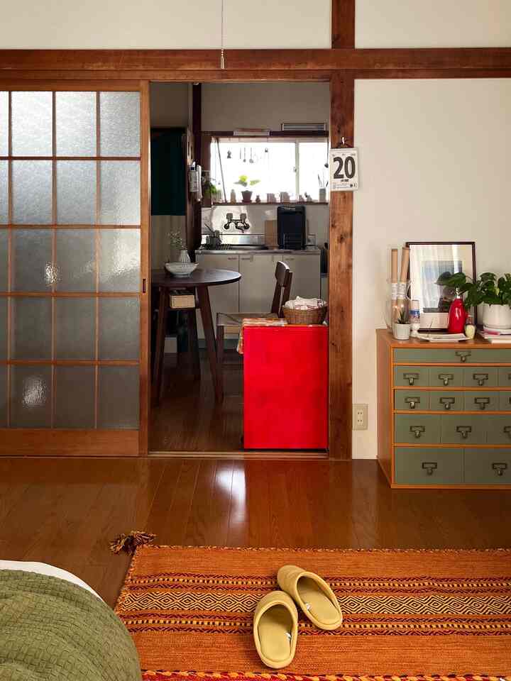 温かみのある木目調と赤のアクセントが特徴的な、小さなキッチンとリビングの空間