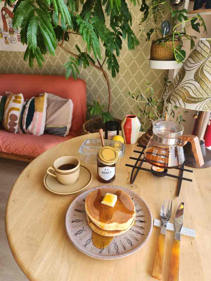ナチュラルな色調のリビングスペース、木製テーブルの上にパンケーキとコーヒーサーバーが置かれた雰囲気のあるおうちカフェ