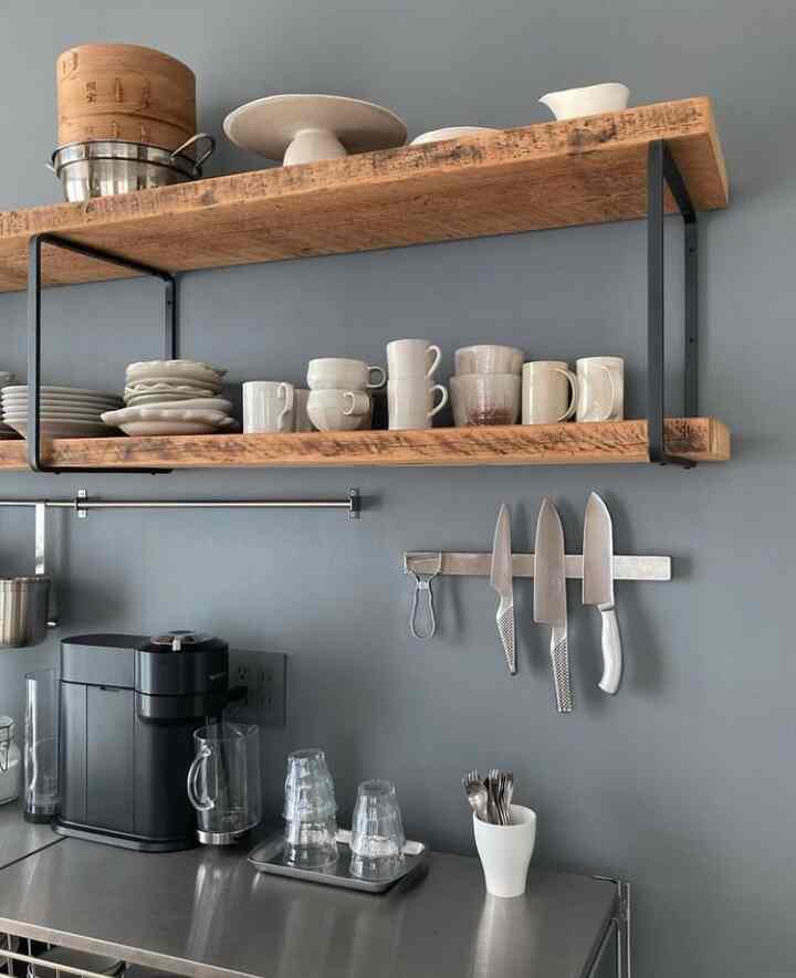 Modern kitchen with gray walls, wooden open shelves, and stainless steel countertop featuring kitchenware and utensils