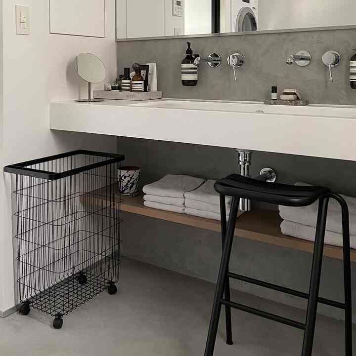 Modern white and black laundry room featuring a large sink, organized storage shelves with towels, and a black stool