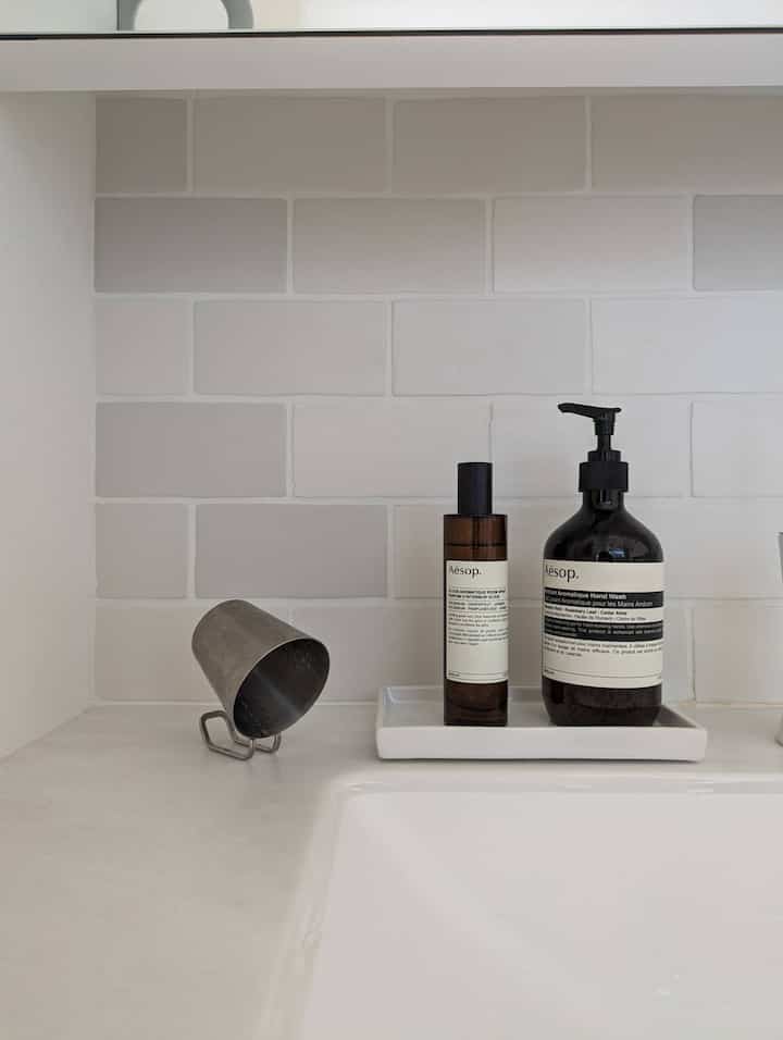 White and gray toned bathroom featuring Aesop hand wash and room spray neatly arranged in a minimal space