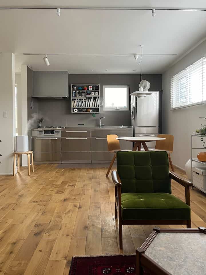 Natural color and wood tone compact kitchen and dining room featuring a green armchair in a warm living area