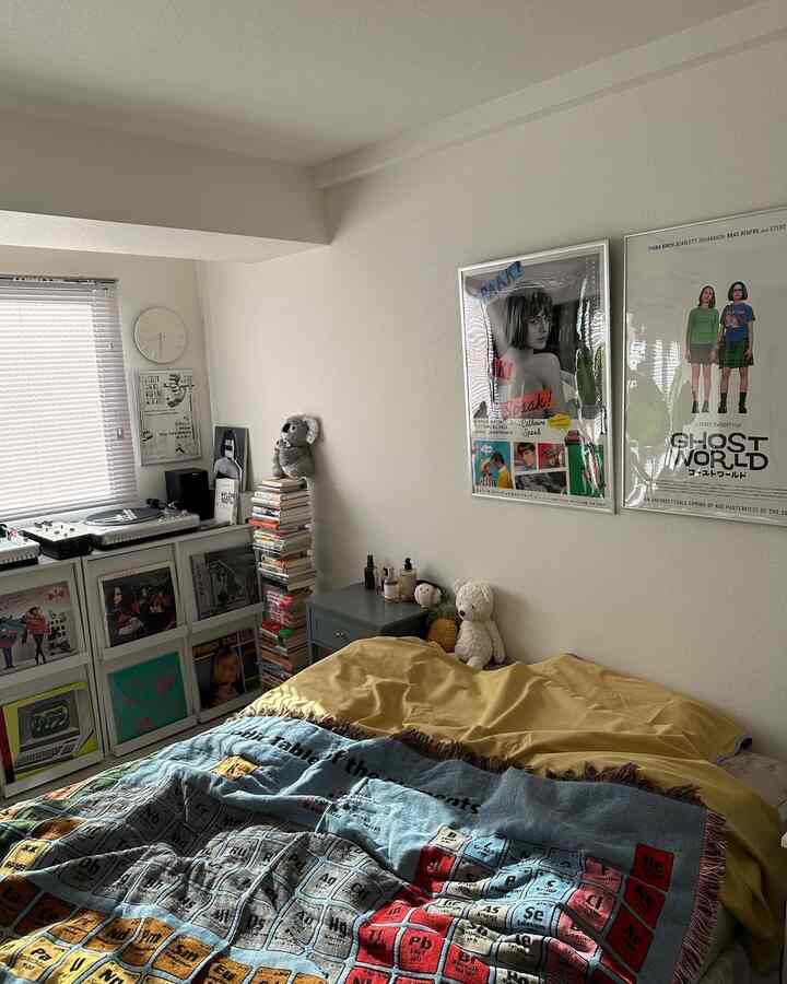 白い壁と天井の寝室、マスタードの掛け布団と元素周期表のスローがあり、本棚とポスターで飾られた雰囲気のあるインテリア