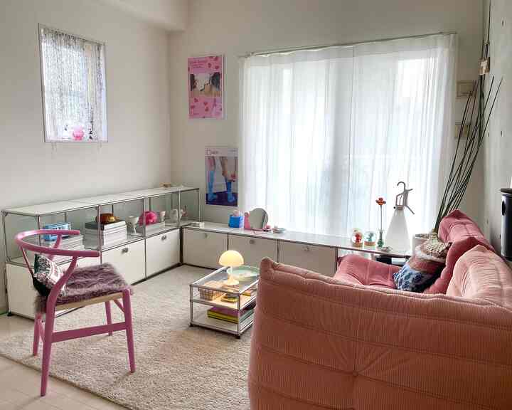 Bright living room in white and pink tones featuring a pink sofa, table lamp, and poster on the wall creating a natural atmosphere