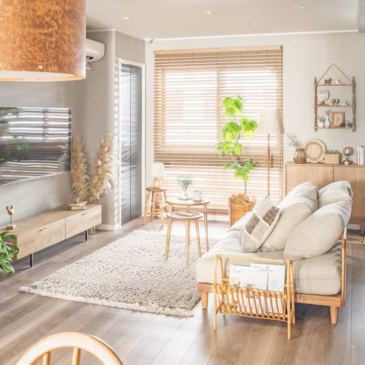 Bright natural-toned living room featuring a three-seater sofa, wooden tables, wood flooring, and blinds creating a cozy atmosphere