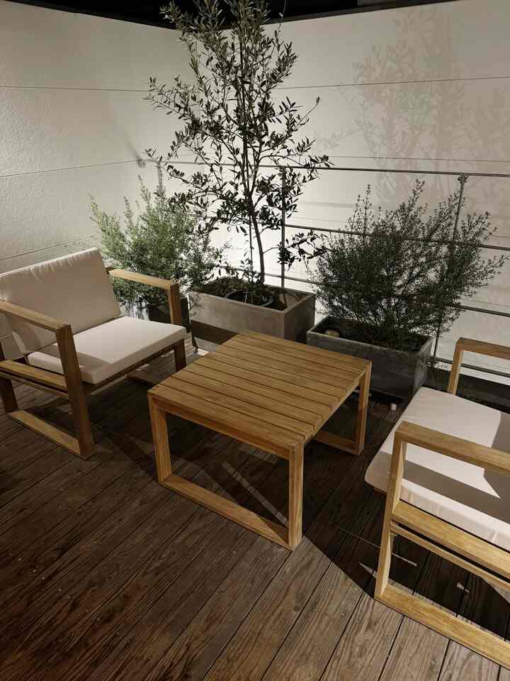 ナチュラルな木目調と白いクッションが調和するバルコニー、快適なアームチェアとサイドテーブルが配置された雰囲気のあるインテリア