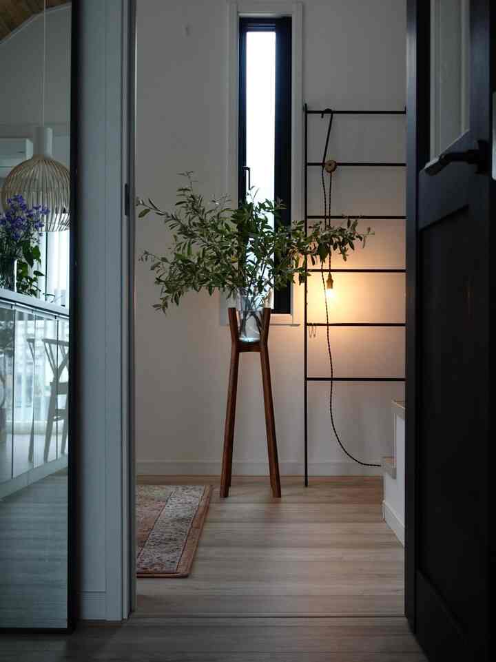 Natural tone entrance space featuring a wooden plant stand and wall sconce lighting with a simple and cozy atmosphere