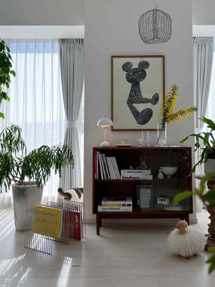 白と茶色のトーンのリビング、黄色いミモザが飾られた透明な花瓶と本棚が配置された雰囲気のあるインテリア