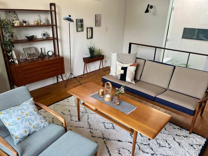 白い壁と茶色の木製家具、ソファとアームチェア、ラグが配置されたスカンジナビアスタイルのリビング空間