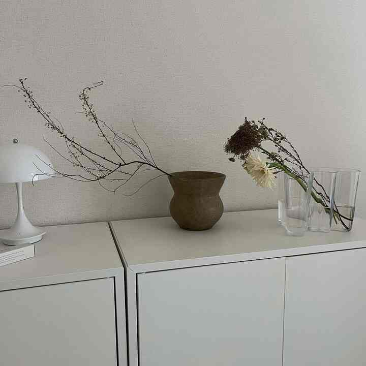 ホワイトのキャビネットの上に置かれたナチュラルなブラウンの花瓶とドライフラワーの枝が配された、シンプルで落ち着いた雰囲気のインテリア
