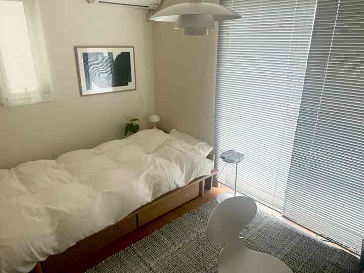 Bright white and wood tone bedroom for single occupancy, featuring minimal furniture and a clean, cozy atmosphere