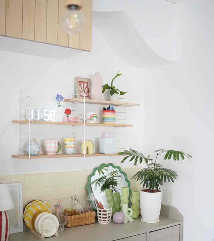白と木目調のキッチンスペース、壁面の棚に様々なカップや植物が配置されたシンプルな雰囲気のインテリア