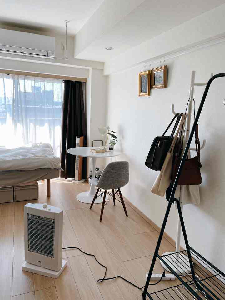 A cozy studio bedroom in white and natural wood tones featuring a round table and grey chair