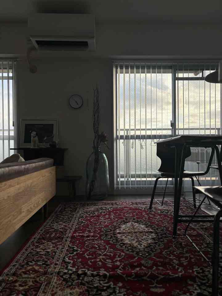 レッドのラグと木目調家具が配置されたミッドセンチュリーモダンのリビング、大きな窓に白い縦型ブラインドがあり明るい雰囲気のインテリア