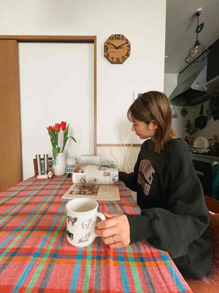 赤と茶色のトーンのキッチン兼ダイニングスペース、中央のテーブルにマグカップとチューリップがあり、女性が雑誌を見ている印象的な空間