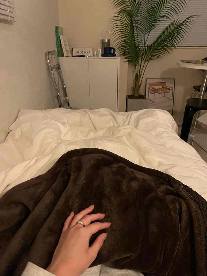 暖かみのあるブラウンとホワイトの寝室、電気毛布の上に手が置かれた居心地の良い空間