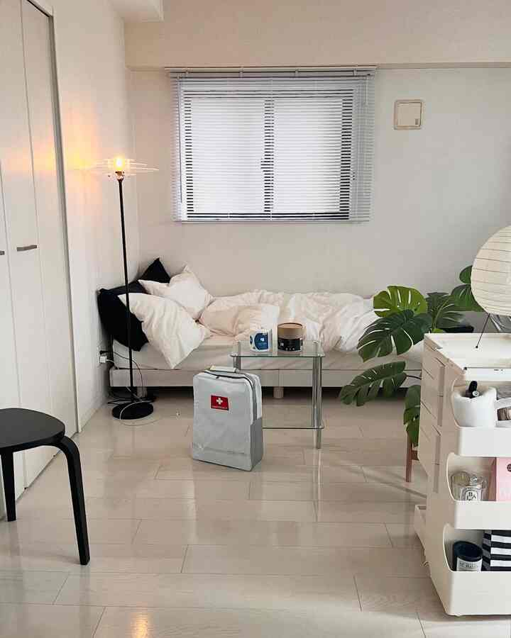 Bright white and natural toned bedroom for a single household featuring a minimalist bed, floor lamp, and green plant