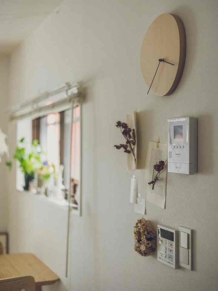 ナチュラルな色調の壁に木製時計と植物が配置された落ち着いたインテリア