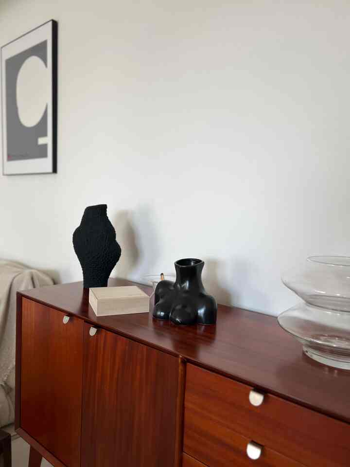 茶色の木製ドレッサーの上に黒いオブジェと透明な花瓶が置かれたシンプルでナチュラルな印象のリビング
