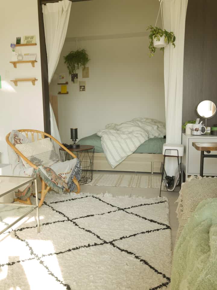 ベージュとホワイトの色調の1LDKのリビング兼寝室、自然素材の家具と植物が配置された落ち着いた雰囲気のインテリア