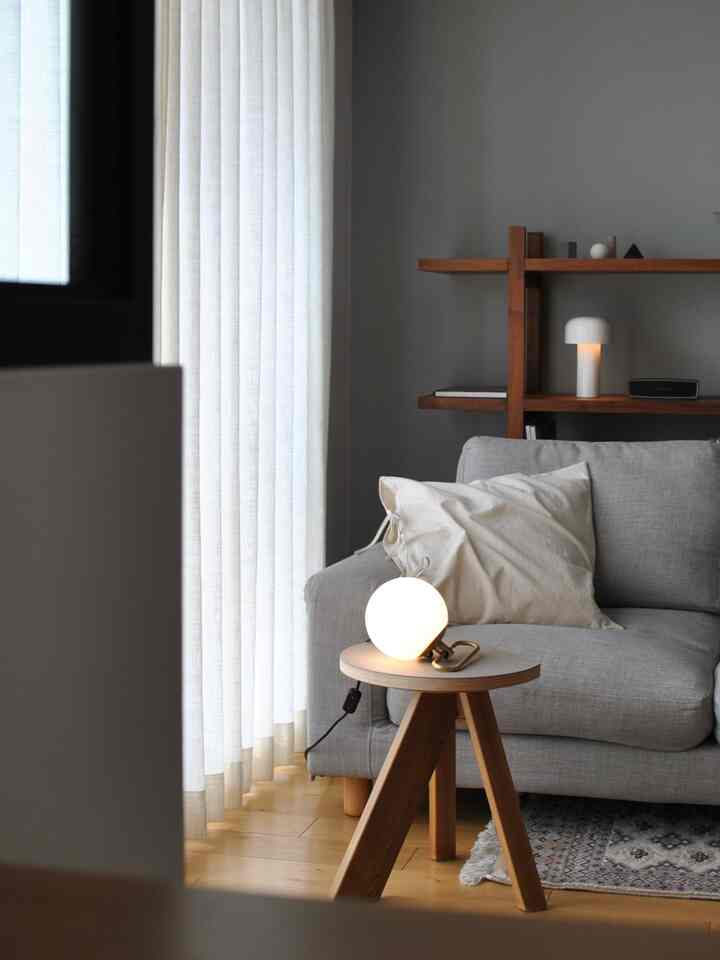 Gray sofa with white cushions in a wood tone and gray harmonious living room, stool with soft glowing lamp creating cozy atmosphere