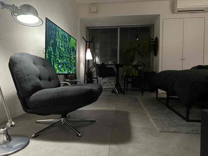 Black and modern toned studio apartment featuring an armchair, bed, desk, and floor lamp arranged in a simple and sleek interior